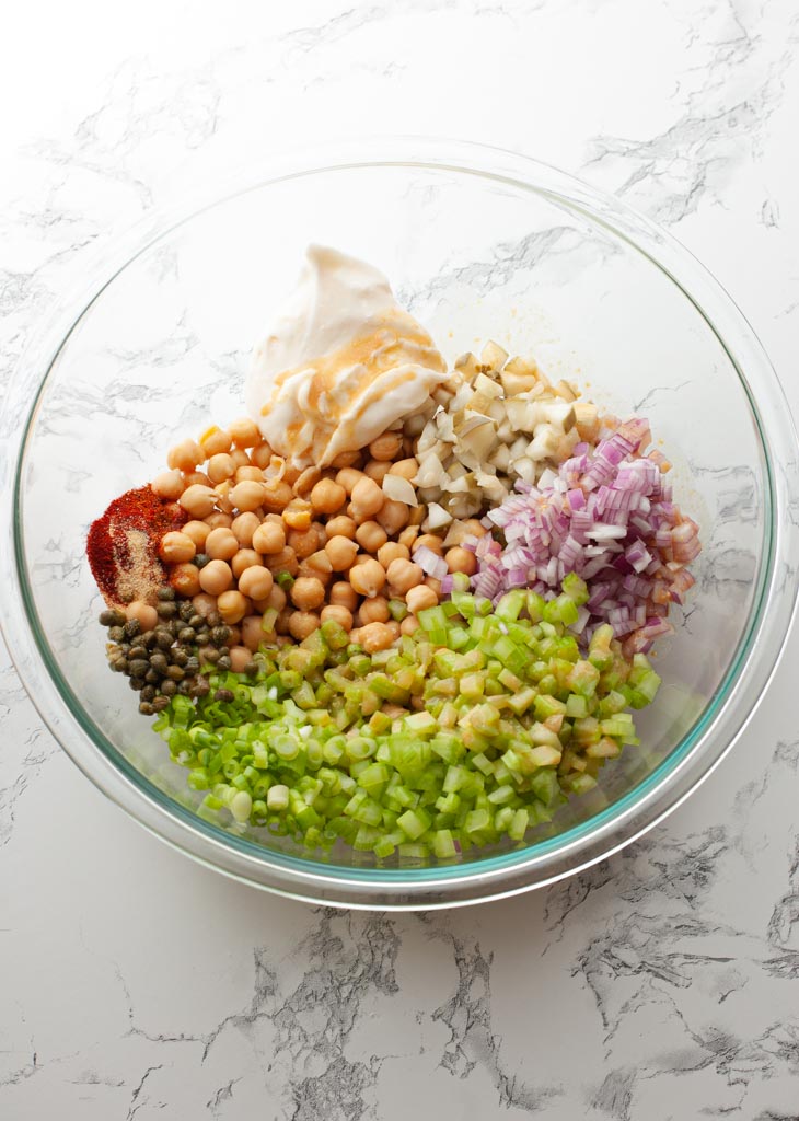 overhead shot of ingridients to make chickpea salad in a clear bowl