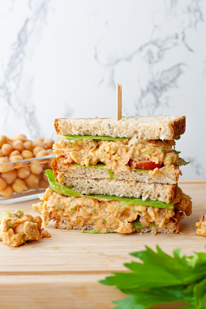 sandwich stacked on a cutting board with a chickpeas in a bowl in the background